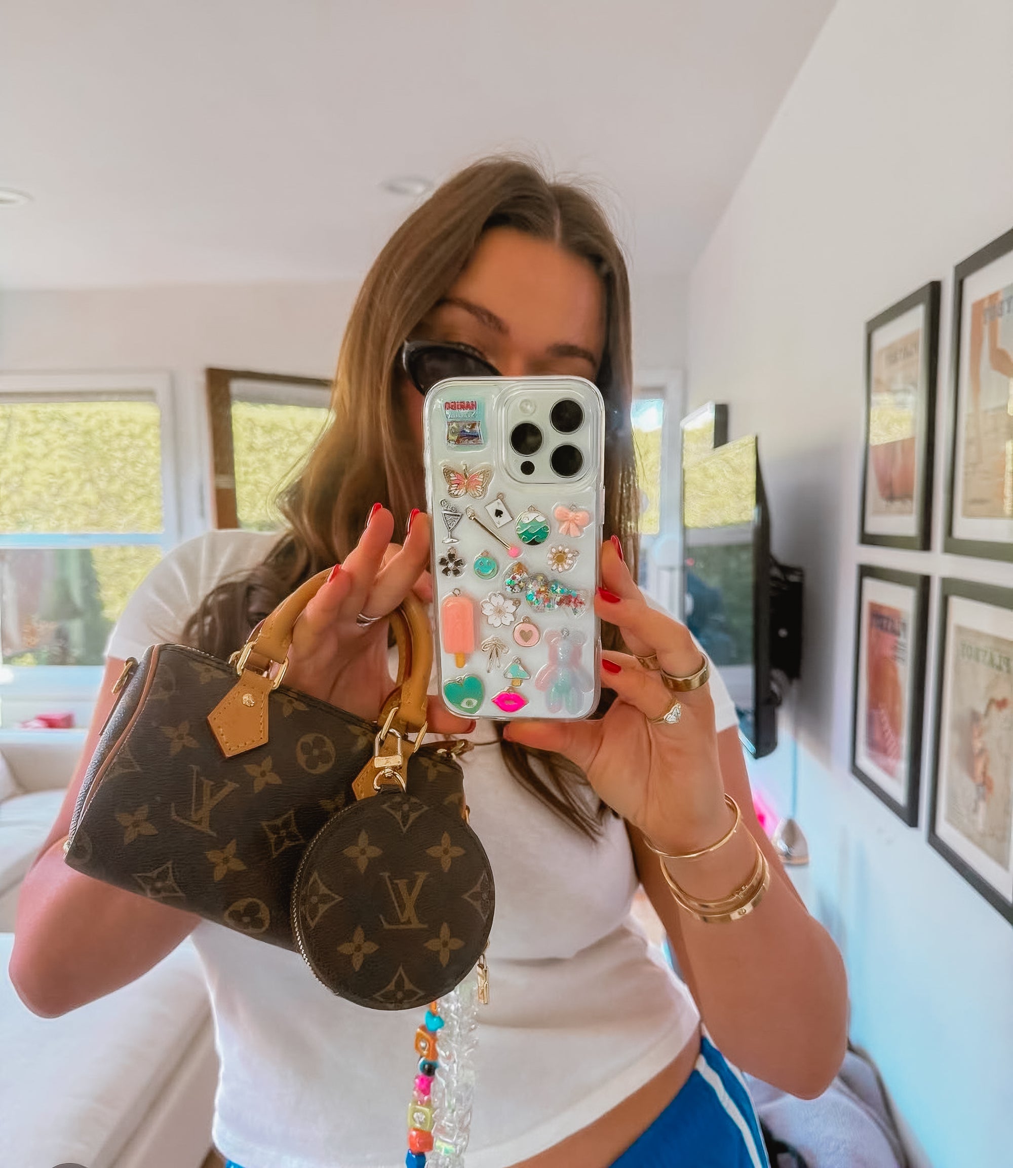 Selfie close-up of a woman holding a custom Shop Chunky phone case decorated with eclectic, colorful charms.