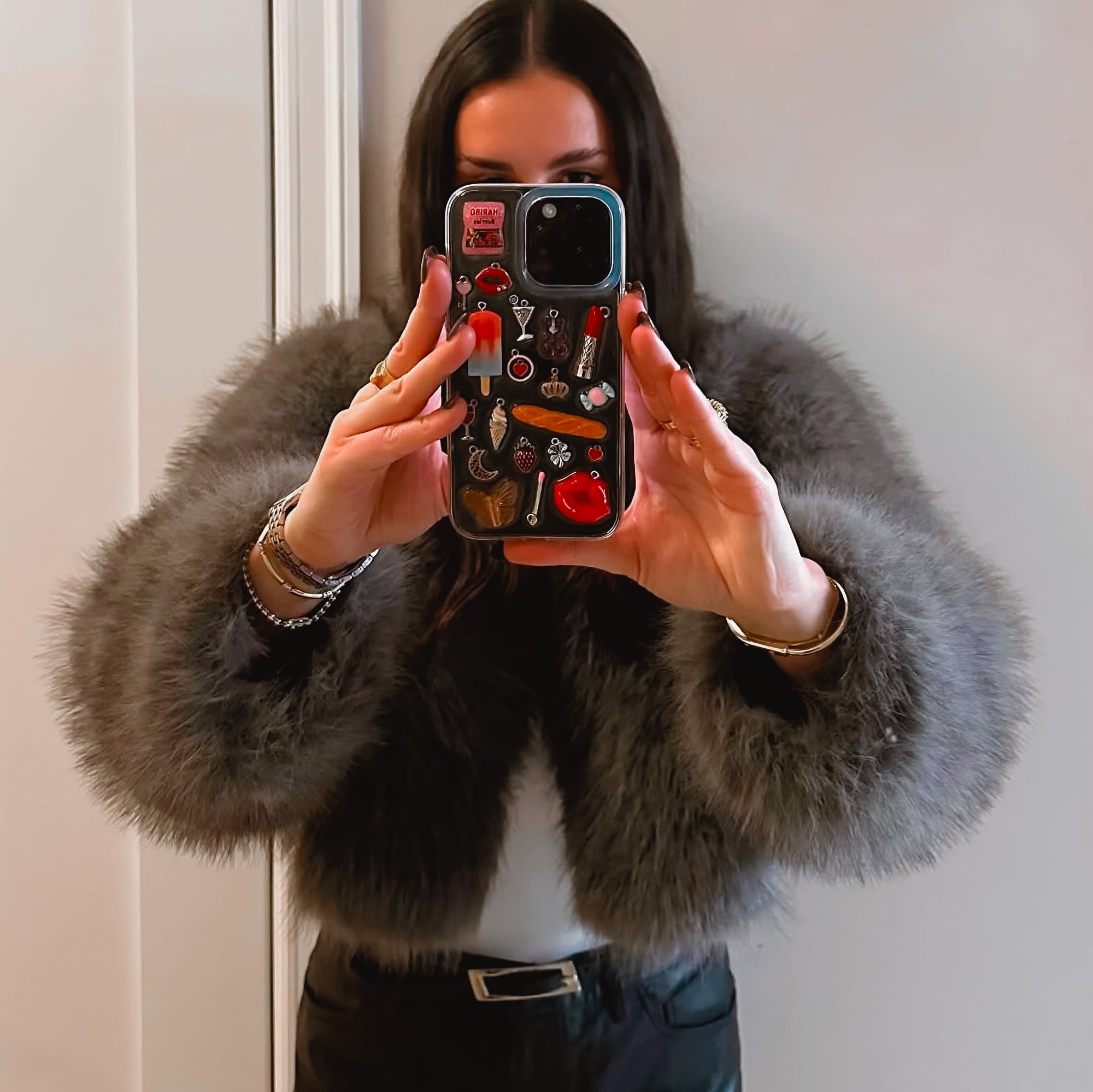Selfie close-up of a woman holding a custom Shop Chunky phone case decorated with eclectic, colorful charms.