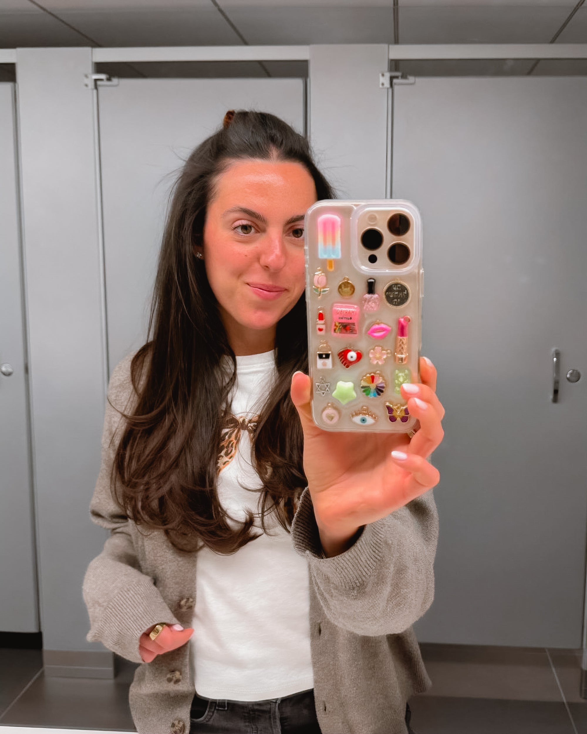Selfie close-up of a woman holding a custom Shop Chunky phone case decorated with eclectic, colorful charms.