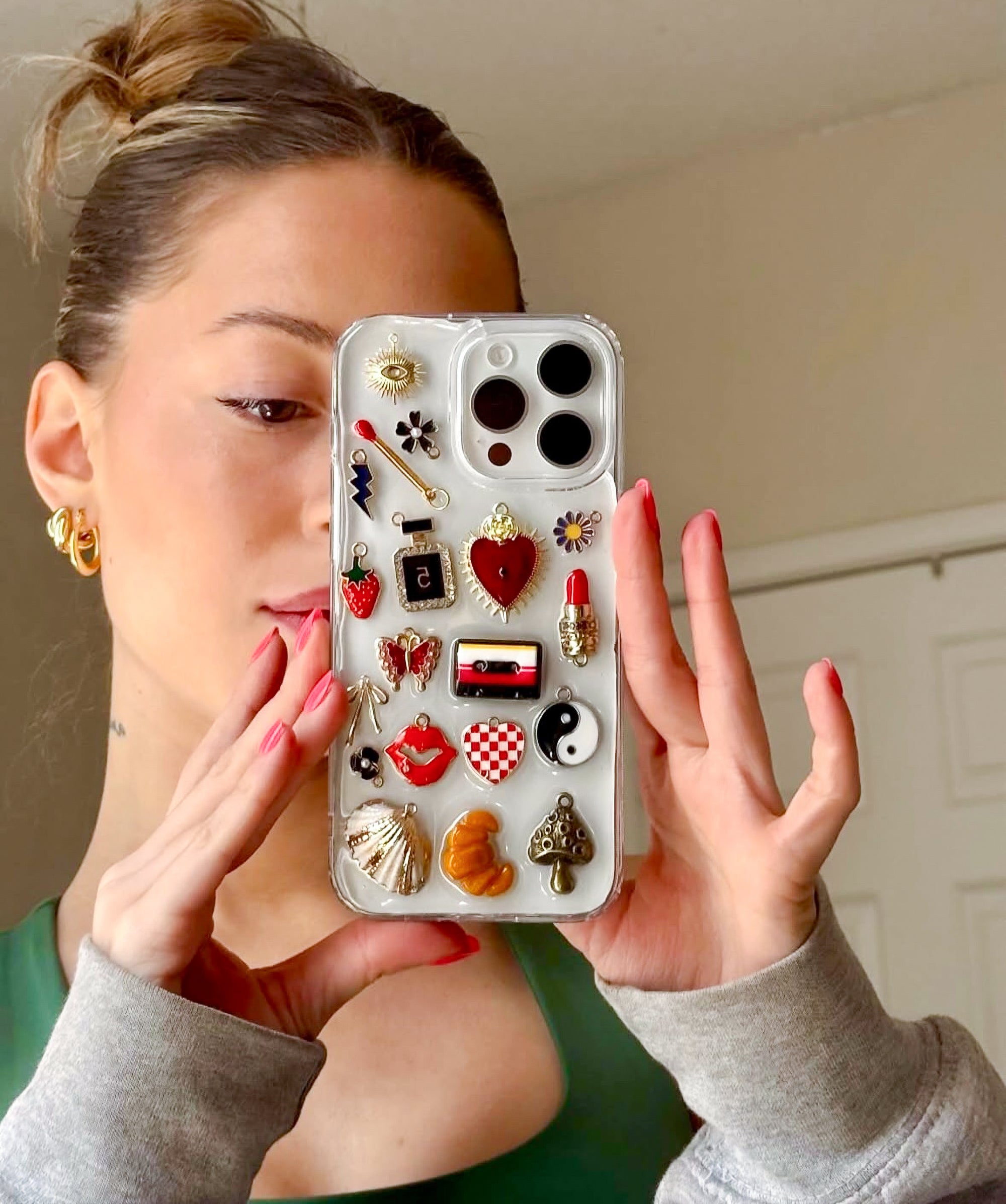 Selfie close-up of a woman holding a custom Shop Chunky phone case decorated with eclectic, colorful charms.