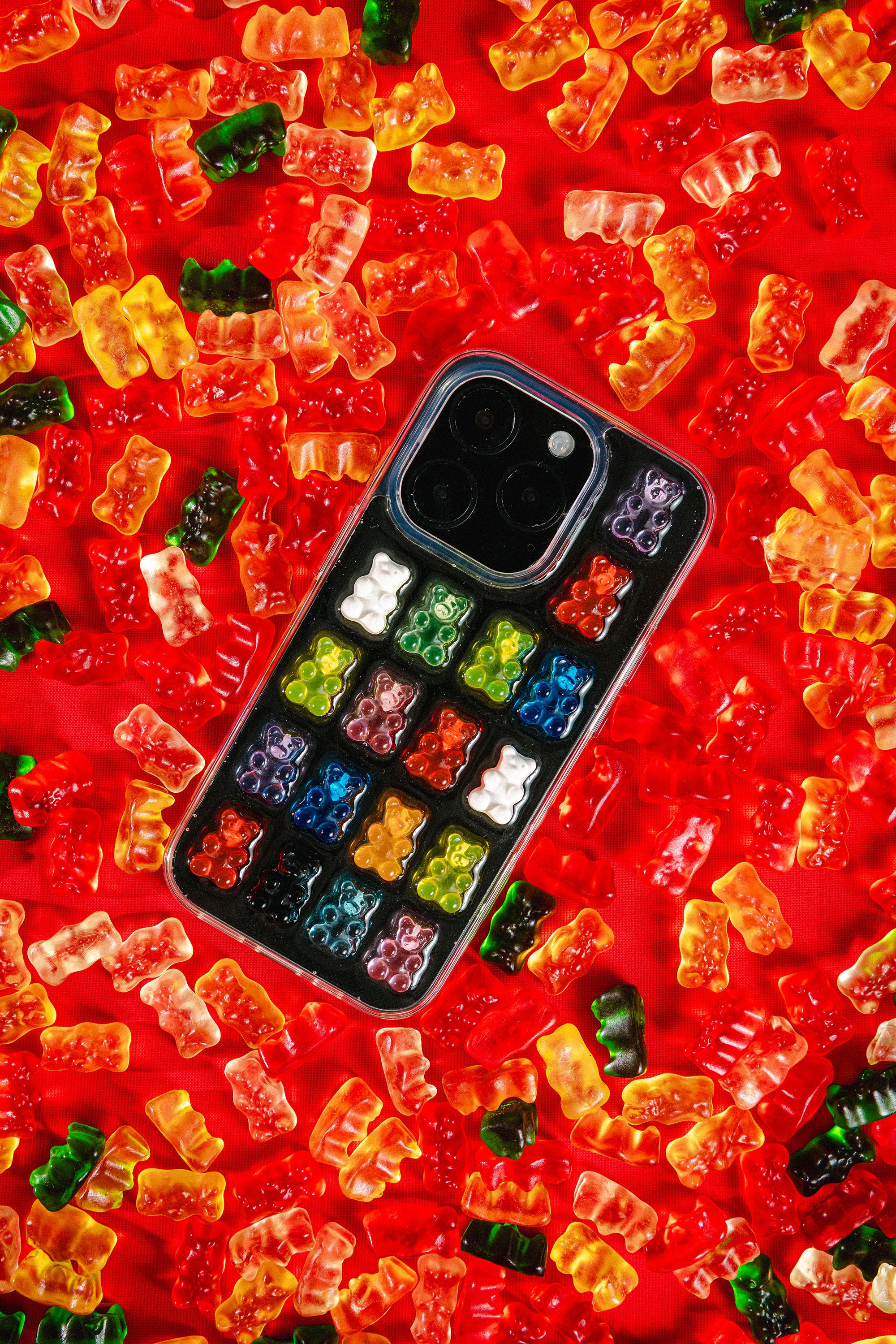 Phone case with colorful bear pattern on a red background laying in a bed of gummy bears